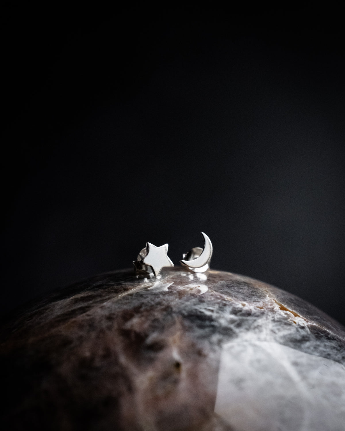 Sterling silver moon and star stud earrings resting on a polished stone sphere