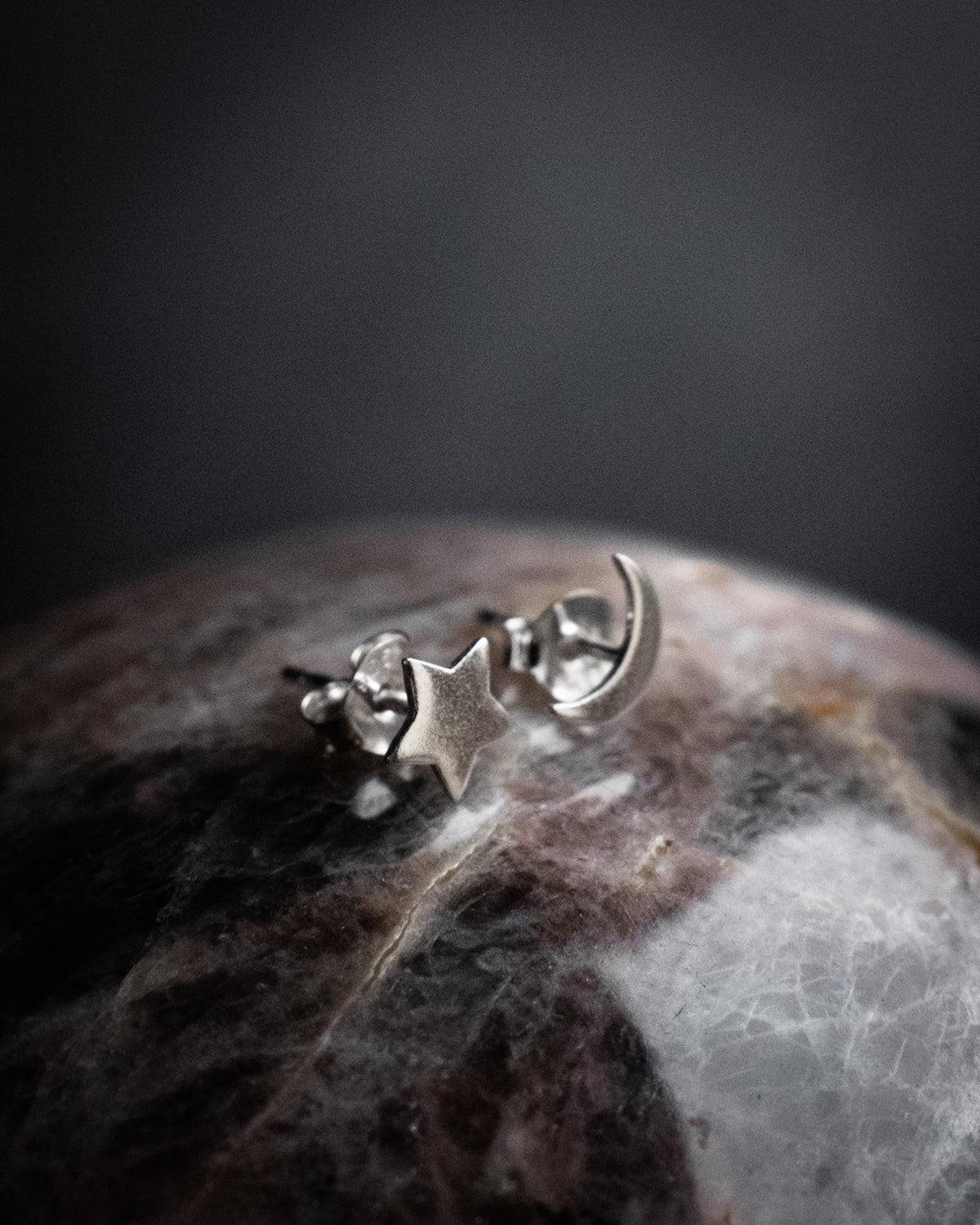 Close-up of sterling silver moon and star stud earrings on a stone sphere