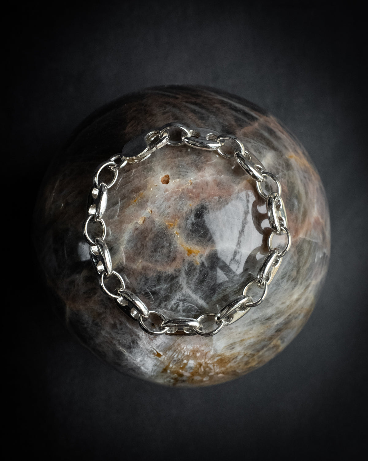 Heavy sterling silver marine chain bracelet laid around a stone sphere