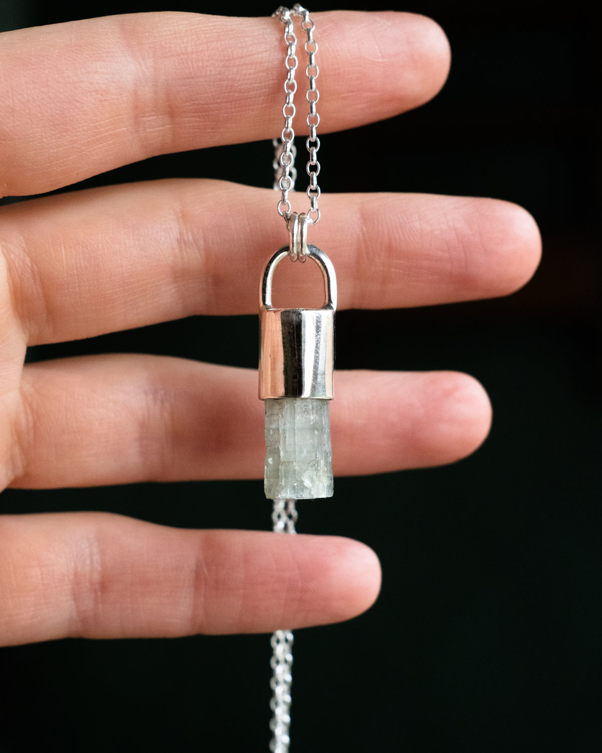 Raw aquamarine sterling silver pendant held in a hand