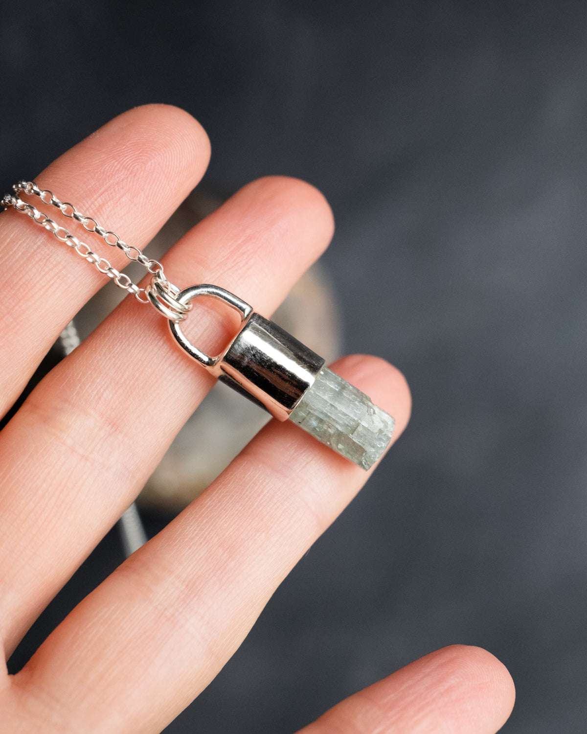 Raw aquamarine sterling silver pendant held between fingers