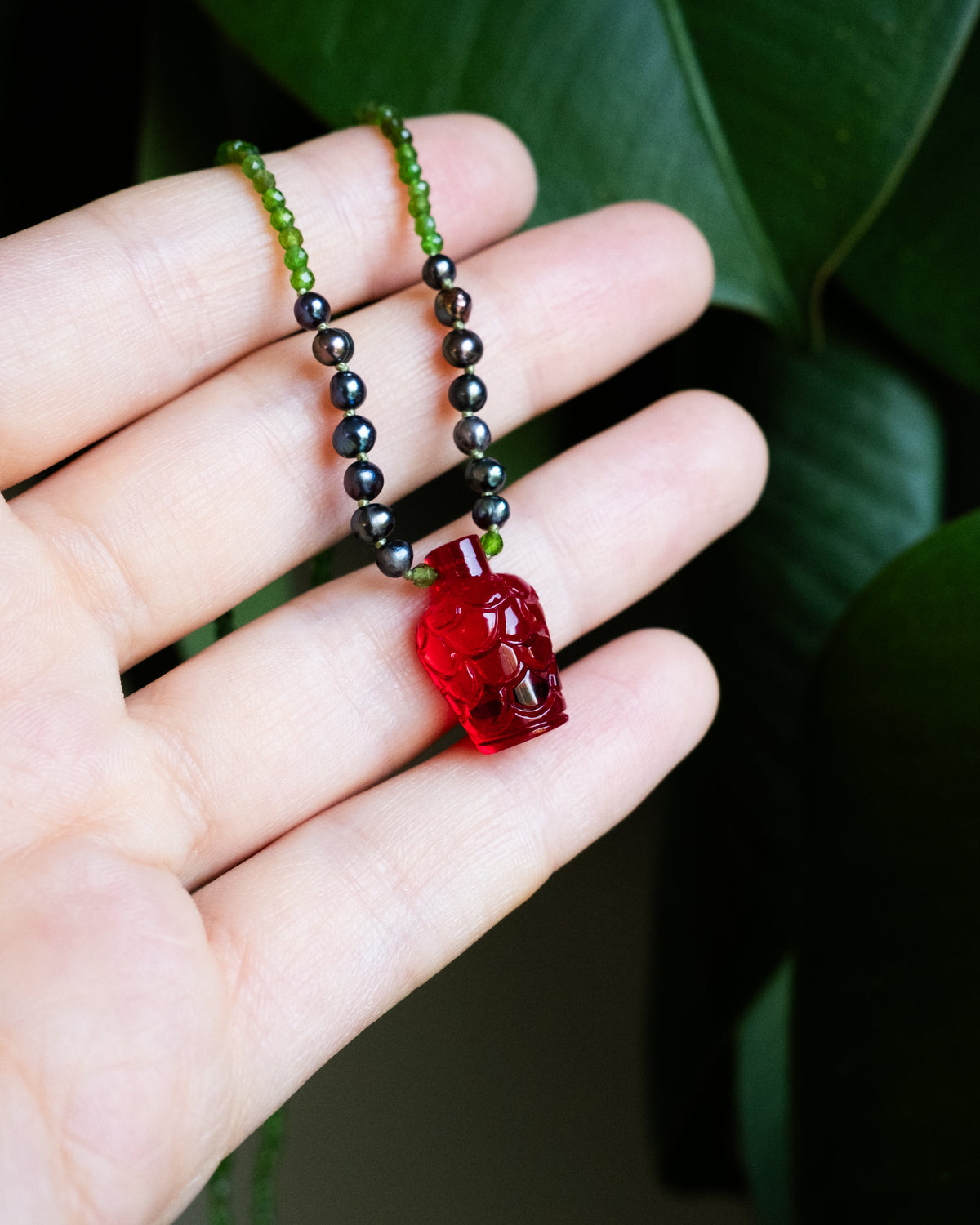 RELIC #009 hand carved red glass bottle necklace with chrome diopside held in a hand