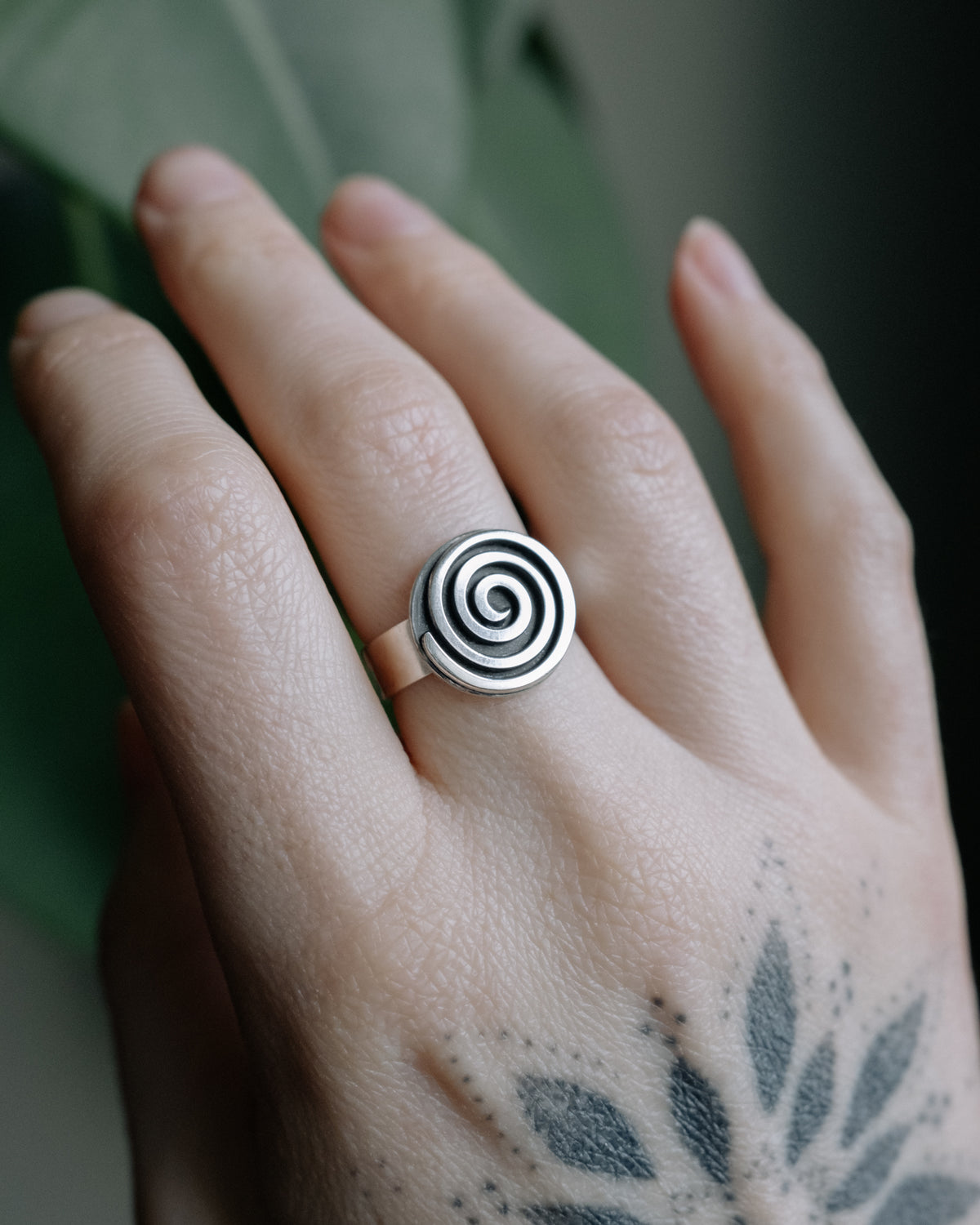 Sterling silver spiral ring worn on a tattooed hand