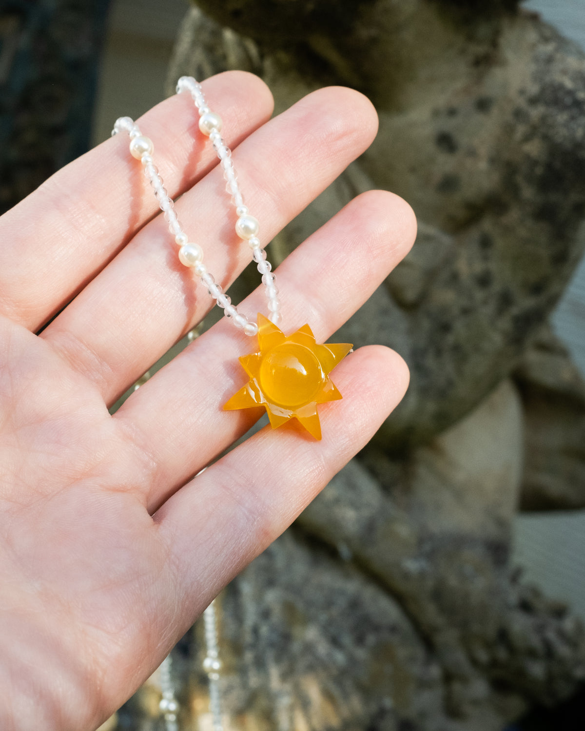 Yellow onyx sun pendant on a clear quartz and opal necklace held in a hand