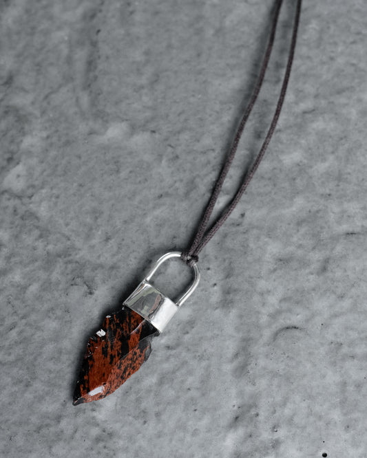 Mahogany obsidian arrowhead set in sterling silver on a brown cord, on grey slate