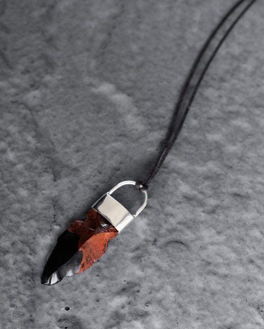 Mahogany obsidian arrowhead set in sterling silver on a brown cord, on grey slate